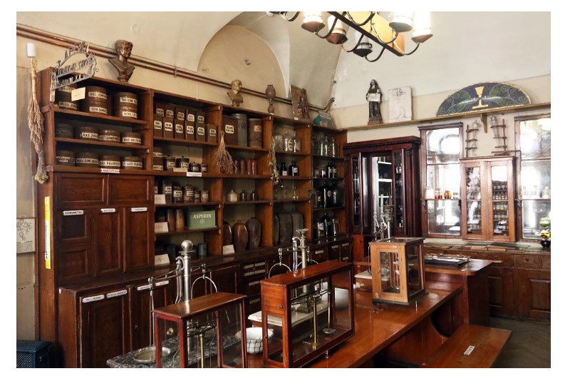 На поличках стоять лікувальні трави, глечики з-під мінеральних вод, а по центру ваги XVIII – XX ст.