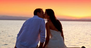 6 липня - Всесвітній день поцілунків couple kissing at sunset sitting in jetty at orange sea lake